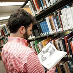 A student reading a book in the library stacks.